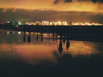 Silhouette city by sea against sky at night