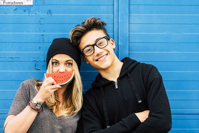 Portrait of young woman with friend holding artificial watermelon against wall