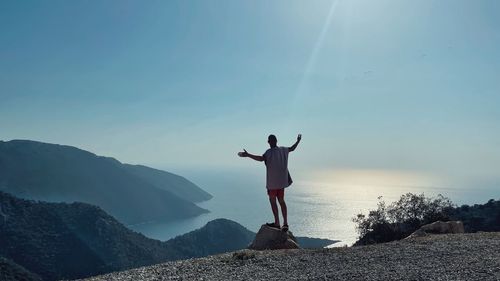 Rear view of man jumping on mountain against sky