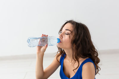 Young woman drinking water from bottle while sitting on table