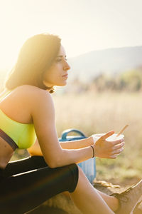 Side view of woman eating food while sitting on land against sky