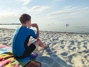 Rear view of boy sitting on beach against sky