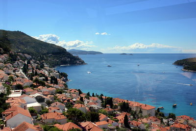 High angle view of city by sea against blue sky seen through glass