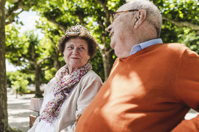 Happy senior couple sitting in park, woman wearing crown