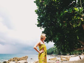 Side view of woman standing by sea against sky