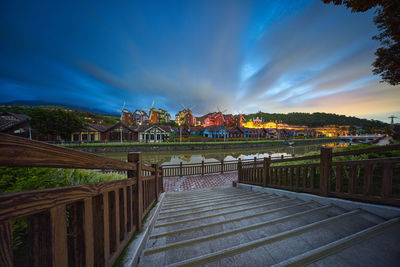 Illuminated footpath by buildings against sky at sunset