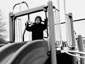 Low angle view of boy standing on slide against sky in playground