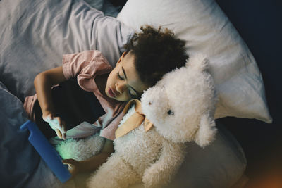 High angle view of boy lying with teddy bear while using digital tablet on bed at home