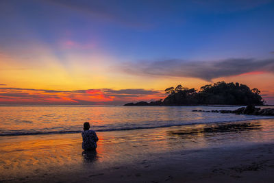 Rear view of man standing on beach during sunset