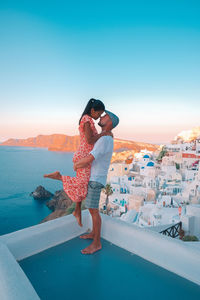 Woman standing  by sea against clear sky, couple on vacation at the greek islands santorini 