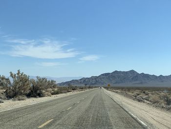 Road leading towards mountains against blue sky