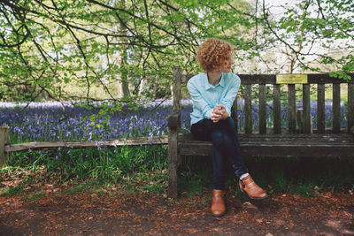 Full length of woman sitting on wooden bench against plants at forest