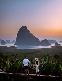 Rear view of couple walking on mountain against sky during sunset