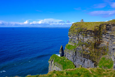 Scenic view of cliff by sea against blue sky