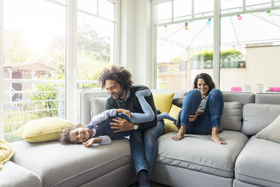 Happy family sitting on couch, father tickling his laughing daughter