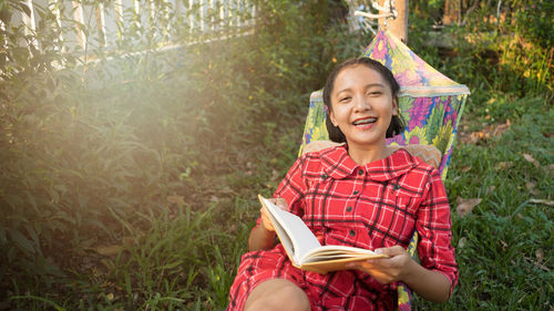 Portrait of smiling teenager reading book at yard