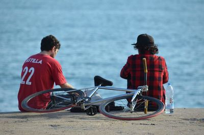 Rear view of men sitting on sea shore