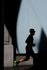 Side view of silhouette man running against wall