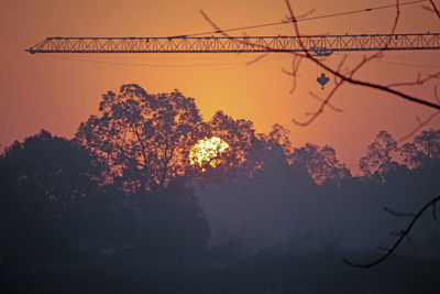 Low angle view of silhouette trees and crane against sky during sunset