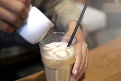 Cropped hands of man preparing iced coffee on table