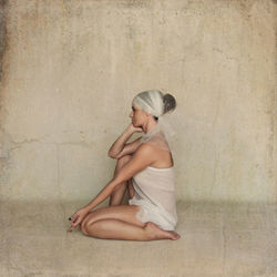 Side view of young woman sitting against wall