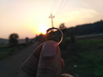 Close-up of man holding sun at sunset