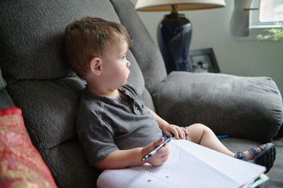 Young boy drawing doodles in a notebook while sitting on a couch at home