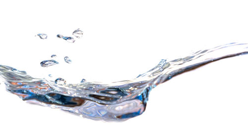 Close-up of drop falling on glass against white background