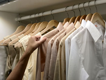Cropped image of man touching clothes hanging on rack