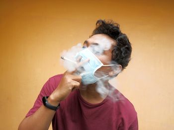 Portrait of young man holding mask against wall