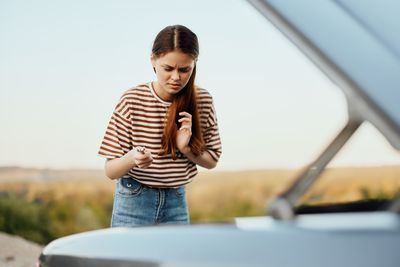 Side view of young woman standing in car