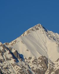 Low angle view of snowcapped mountains against clear blue sky