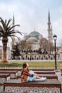 Woman sitting outside temple against sky