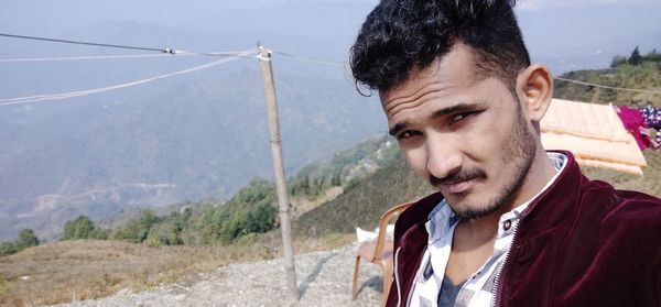 Portrait of young man looking at mountains against sky