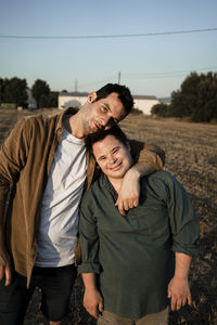 Man standing with arm around friend at stubble field