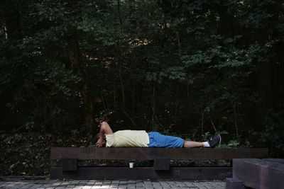 Side view of man lying on bench against plants