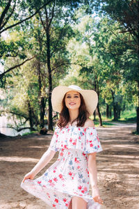 Beautiful girl in a hat and dress with floral print on the street in summer
