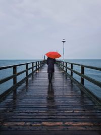 Rear view of woman standing on pier at sea during rainy season