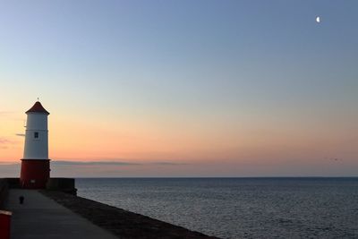 Lighthouse by sea against clear sky during sunset