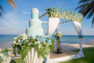 Close-up of flower vase on beach against blue sky