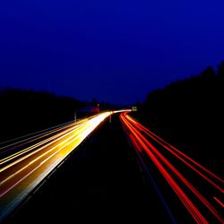 Light trails on road against clear blue sky at night