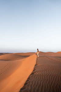Rear view of man walking on sand dune in desert against clear sky