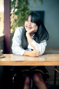 Smiling young girl looking away while sitting by table