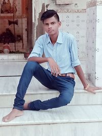 Portrait of young man sitting against wall