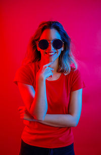 Young woman wearing sunglasses against red background