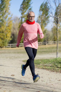 Senior man running on sand against trees