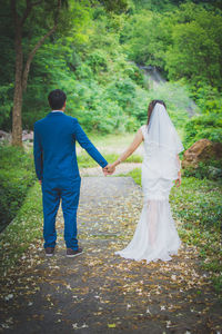 Rear view of bride and groom standing on pathway in forest