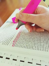 Cropped hand marking with pink highlighter in book