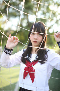 Portrait of young woman standing by sports net