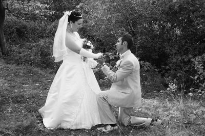 Side view of groom proposing bride during wedding ceremony against plants